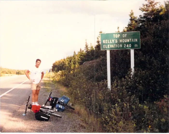 Man next to a sign saying top of kelly's mountain